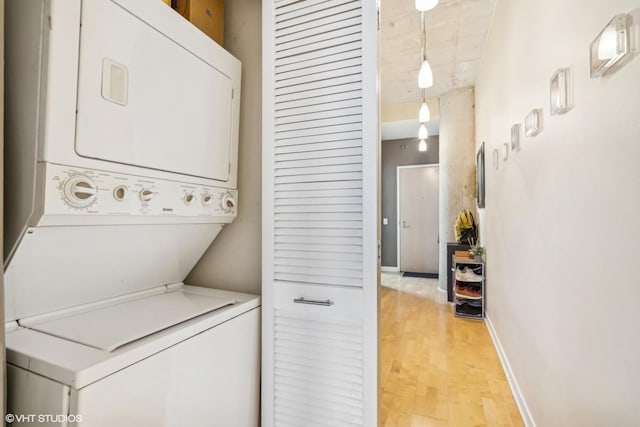 washroom with baseboards, light wood-style floors, stacked washer / dryer, and laundry area