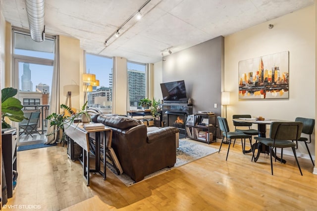 living room featuring rail lighting, expansive windows, a lit fireplace, light wood finished floors, and a city view