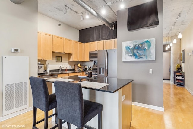 kitchen featuring dark countertops, appliances with stainless steel finishes, a sink, a high ceiling, and light brown cabinetry