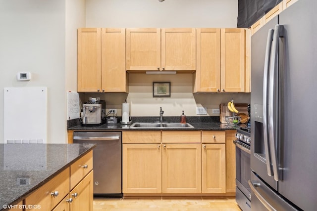 kitchen featuring a sink, dark stone countertops, appliances with stainless steel finishes, and light brown cabinets
