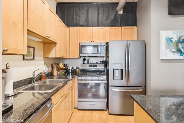 kitchen with a sink, light brown cabinetry, light wood-type flooring, and appliances with stainless steel finishes