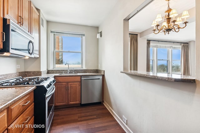 kitchen with brown cabinetry, appliances with stainless steel finishes, a healthy amount of sunlight, a sink, and a notable chandelier