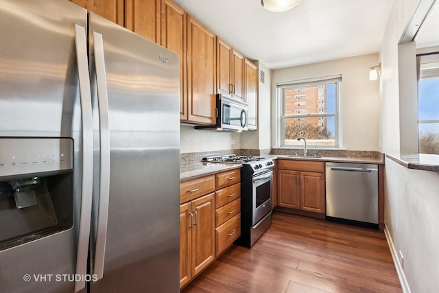 kitchen with a sink, dark wood finished floors, brown cabinetry, stainless steel appliances, and stone countertops