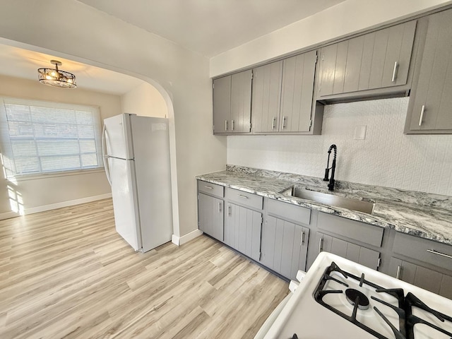 kitchen featuring tasteful backsplash, white appliances, gray cabinets, a sink, and light wood-style floors