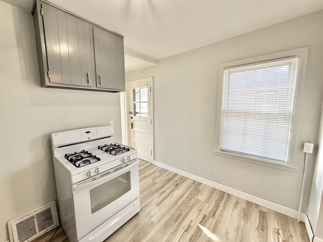 kitchen featuring visible vents, light wood-style flooring, white gas range, baseboards, and gray cabinets