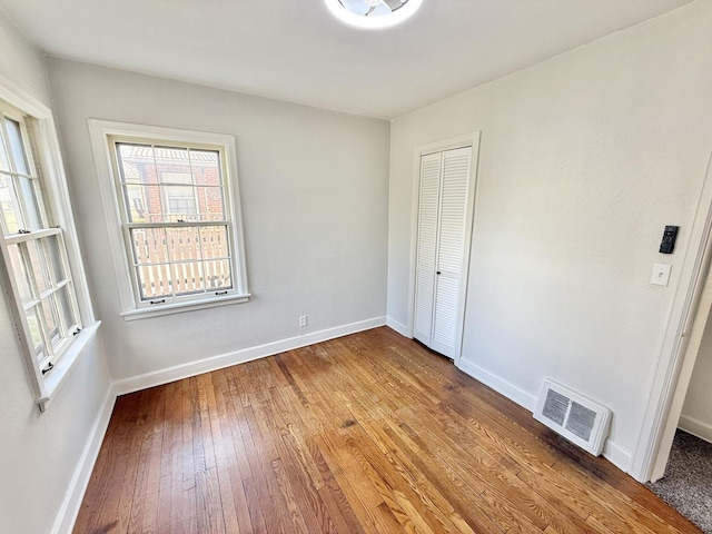 unfurnished bedroom with a closet, baseboards, visible vents, and wood-type flooring