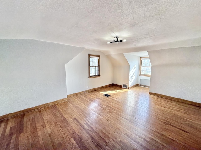 bonus room with a textured ceiling, lofted ceiling, light wood-style flooring, baseboards, and visible vents