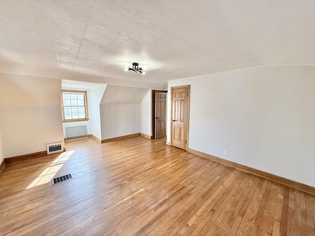 additional living space featuring baseboards, visible vents, light wood-type flooring, and a textured ceiling