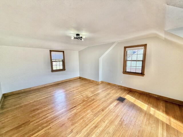 additional living space featuring a textured ceiling, lofted ceiling, plenty of natural light, visible vents, and light wood-style floors