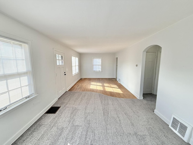 carpeted spare room with arched walkways, baseboards, and visible vents