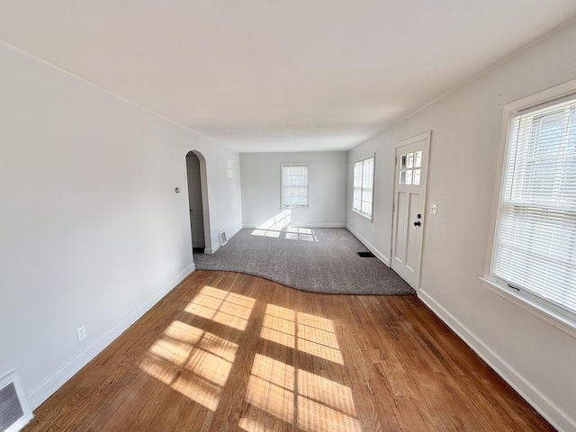 interior space featuring arched walkways, baseboards, visible vents, and hardwood / wood-style floors
