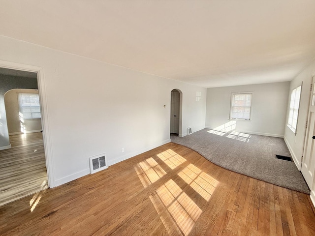 spare room featuring hardwood / wood-style floors, arched walkways, baseboards, and visible vents