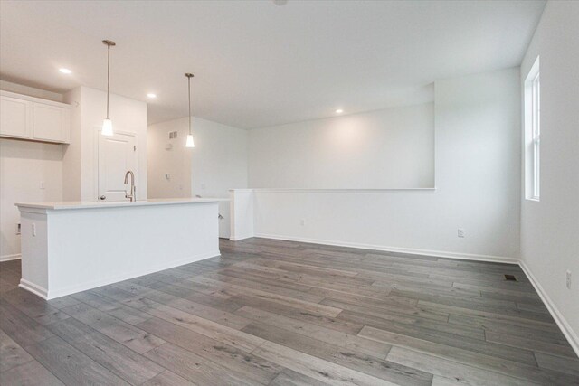 unfurnished living room featuring baseboards, wood finished floors, recessed lighting, and a sink