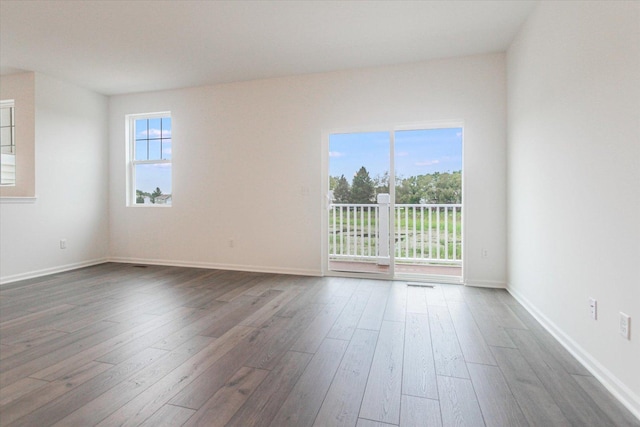spare room featuring dark wood-type flooring, a healthy amount of sunlight, and baseboards
