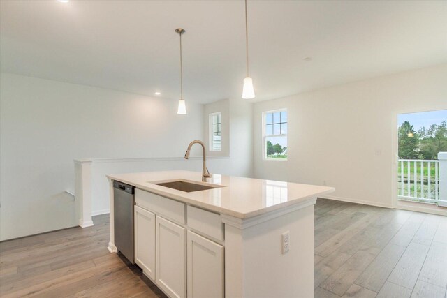 kitchen with a sink, pendant lighting, light wood finished floors, dishwasher, and a kitchen island with sink
