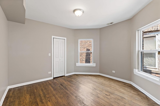 unfurnished room with visible vents, dark wood-style floors, and baseboards