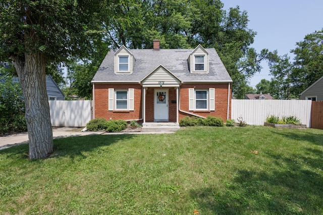 cape cod-style house featuring roof with shingles, brick siding, a front yard, and fence