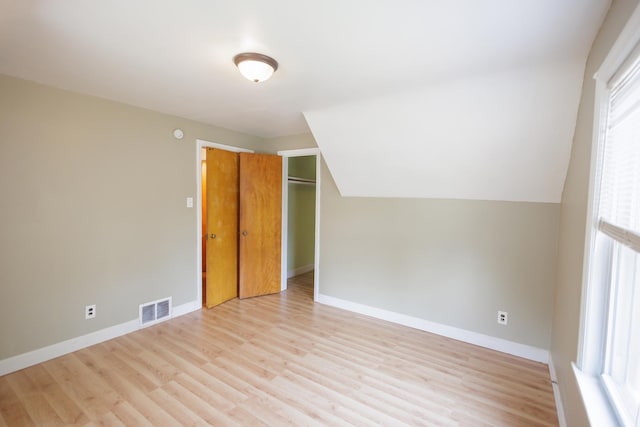 additional living space with baseboards, visible vents, light wood-style floors, and lofted ceiling