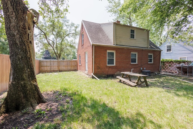 back of house featuring roof with shingles, a chimney, brick siding, a fenced backyard, and a yard