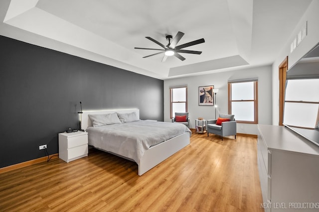 bedroom with light wood finished floors, baseboards, ceiling fan, and a raised ceiling
