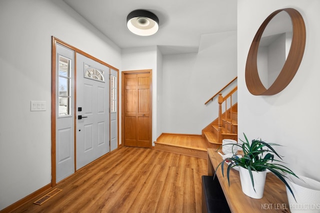 foyer entrance with stairs, baseboards, light wood finished floors, and visible vents