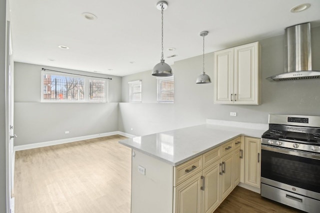 kitchen featuring cream cabinetry, wood finished floors, wall chimney exhaust hood, stainless steel range with gas cooktop, and decorative light fixtures