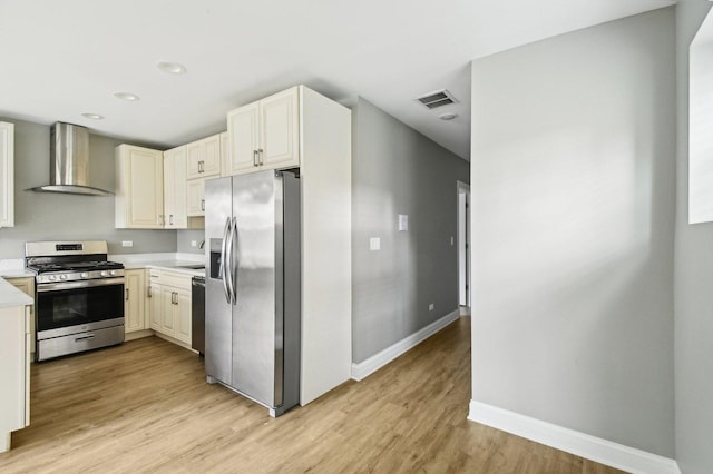 kitchen with light countertops, stainless steel appliances, light wood-style floors, visible vents, and wall chimney range hood