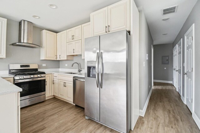 kitchen with a sink, wall chimney exhaust hood, appliances with stainless steel finishes, visible vents, and light wood-style floors