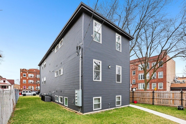 rear view of house featuring a fenced backyard, central AC unit, and a yard