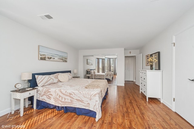 bedroom with baseboards, visible vents, and wood finished floors