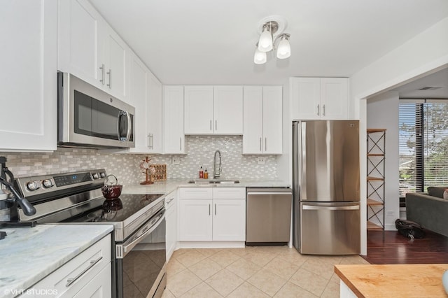 kitchen with white cabinets, tasteful backsplash, a sink, appliances with stainless steel finishes, and light tile patterned floors