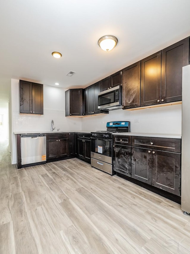 kitchen featuring light countertops, stainless steel appliances, dark brown cabinets, a sink, and light wood-type flooring