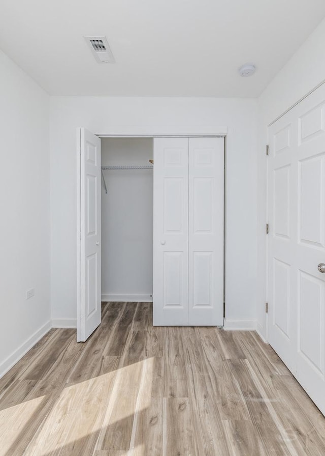 unfurnished bedroom featuring light wood finished floors, baseboards, visible vents, and a closet