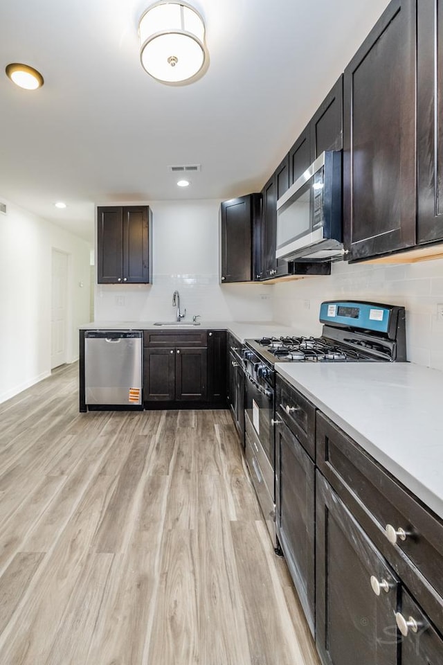 kitchen with decorative backsplash, a sink, visible vents, light wood-style flooring, and appliances with stainless steel finishes