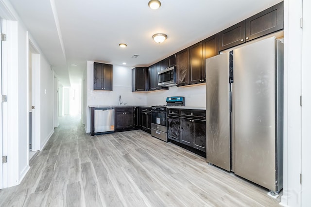 kitchen featuring baseboards, stainless steel appliances, dark brown cabinetry, a sink, and light wood-type flooring