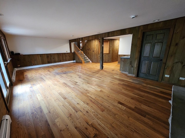 unfurnished living room featuring a baseboard heating unit, wood walls, wood finished floors, and stairs