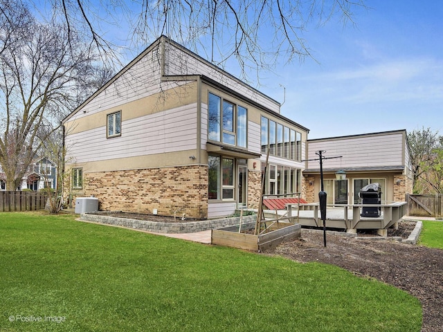 rear view of house featuring brick siding, a yard, a deck, and fence private yard