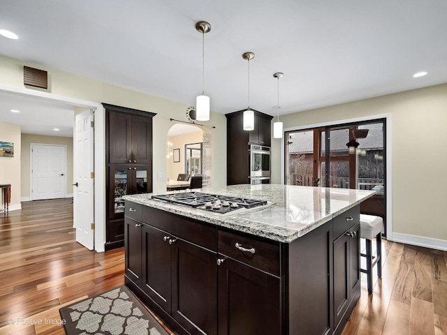 kitchen with arched walkways, appliances with stainless steel finishes, dark wood-style floors, and light stone counters
