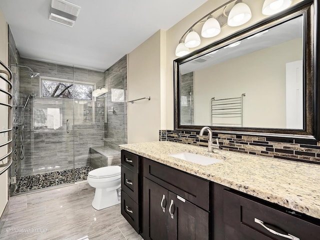 bathroom featuring visible vents, toilet, vanity, decorative backsplash, and a stall shower