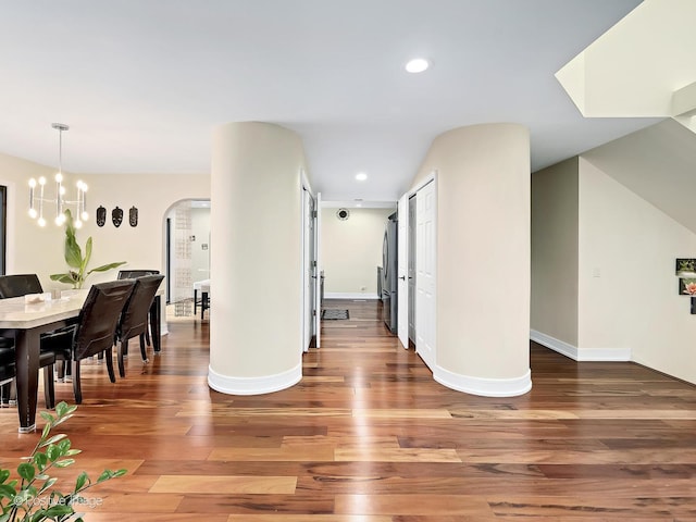 hallway featuring baseboards, arched walkways, wood finished floors, and recessed lighting
