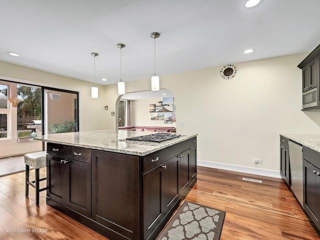 kitchen featuring light stone counters, dark brown cabinets, wood finished floors, arched walkways, and stainless steel appliances