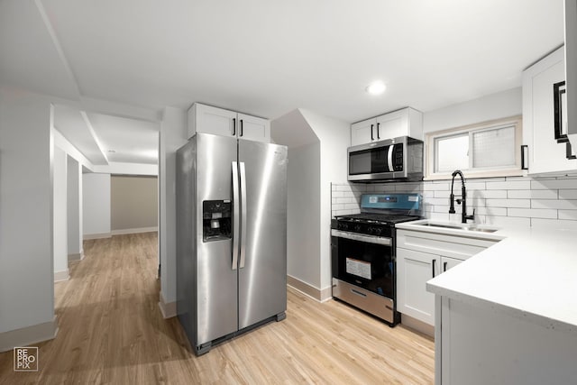 kitchen with a sink, backsplash, white cabinetry, light wood-style flooring, and stainless steel appliances