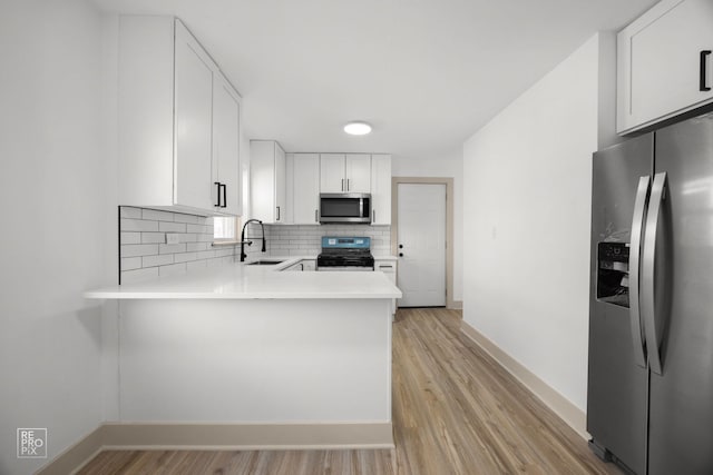 kitchen featuring light countertops, backsplash, a sink, light wood finished floors, and stainless steel appliances