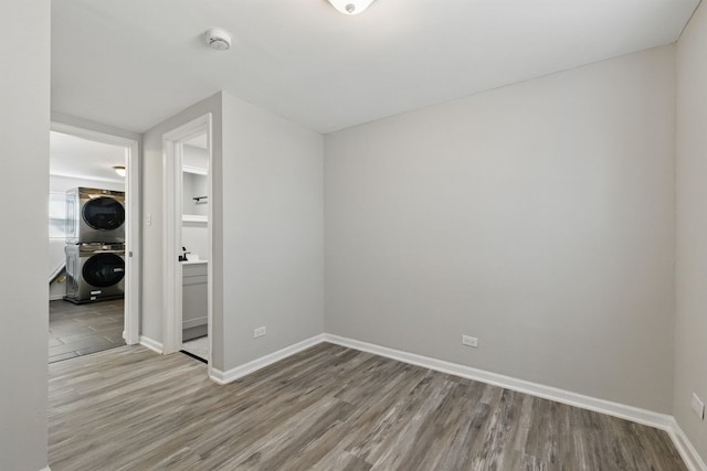 empty room featuring baseboards, wood finished floors, and stacked washing maching and dryer