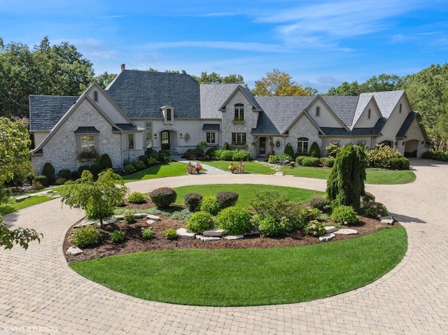 french provincial home with curved driveway, a front lawn, stone siding, and stucco siding