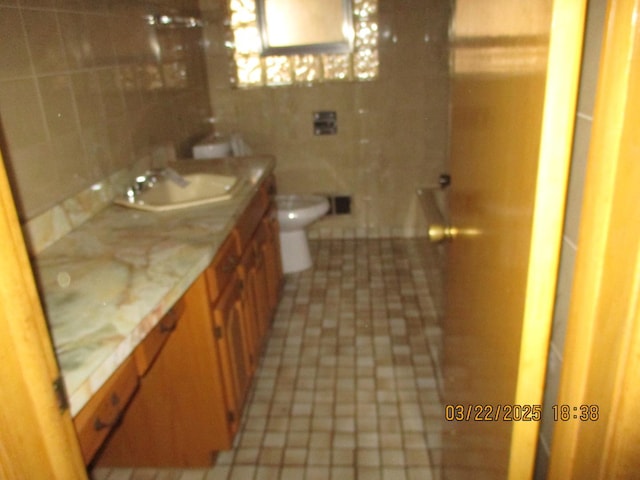 bathroom featuring tile walls, toilet, backsplash, a sink, and double vanity