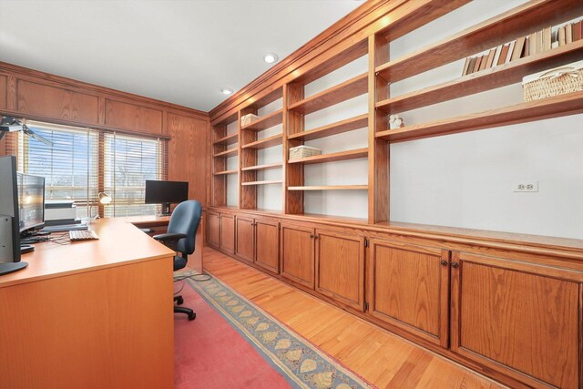 office featuring light wood-type flooring, wood walls, and built in shelves
