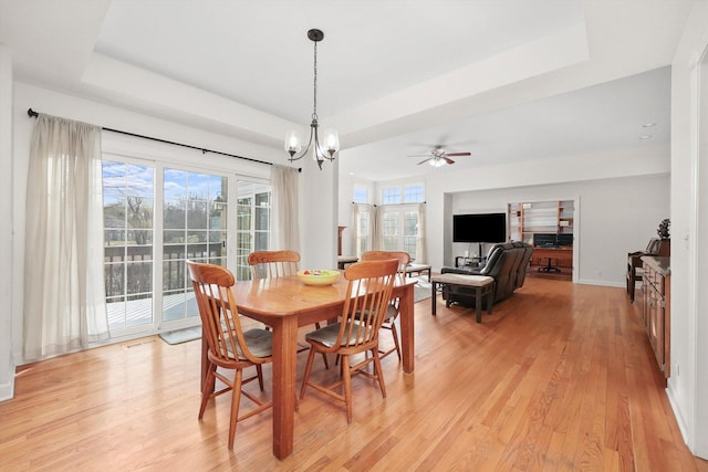dining area featuring a raised ceiling, light wood-style flooring, baseboards, ceiling fan with notable chandelier, and visible vents