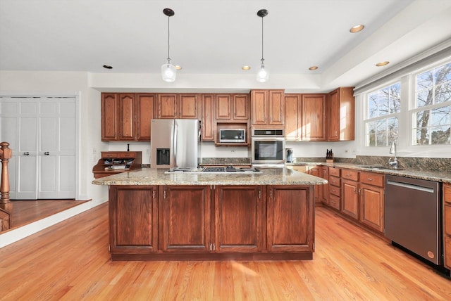 kitchen with a sink, stainless steel appliances, light wood-style floors, and a center island
