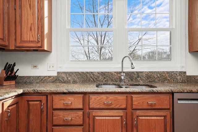 kitchen featuring dishwasher, a sink, dark stone counters, and brown cabinets